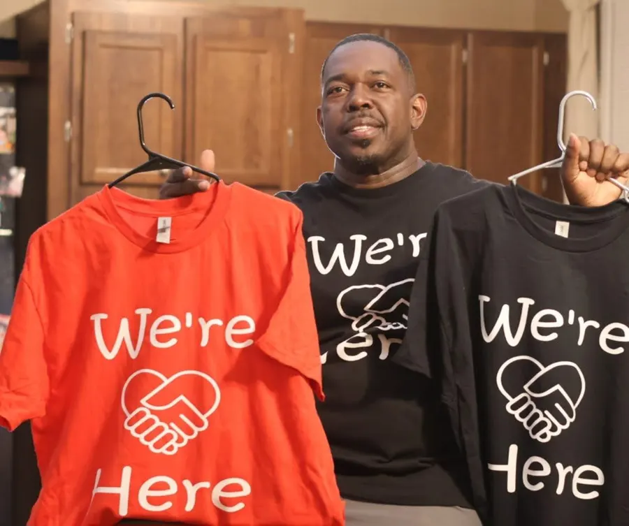 Founder Patrick White holding red and black We're Here T-shirts